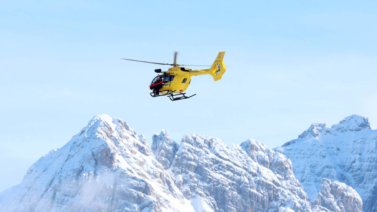 Ż&oacute;łty helikopter ratunkowy w locie nad zaśnieżonymi g&oacute;rami.