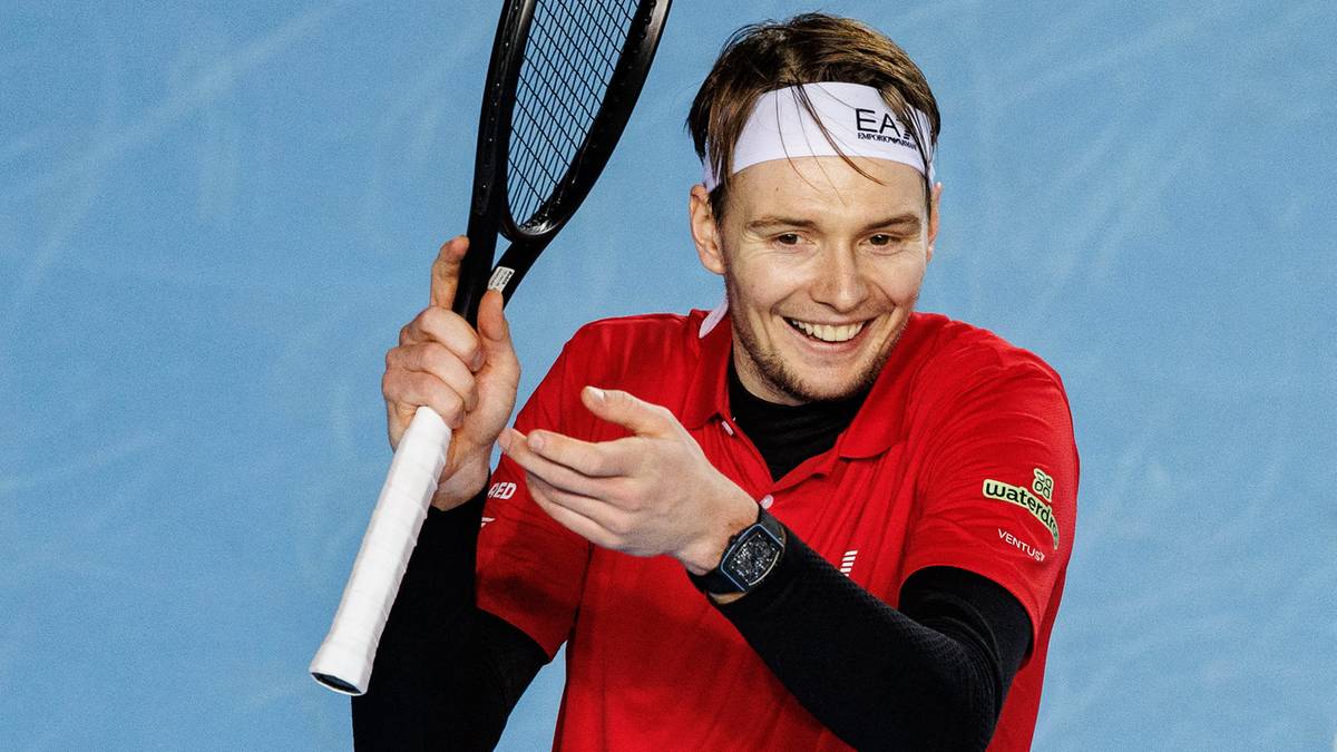 Aleksander Bublik trzyma rakietę tenisową i uśmiecha się.