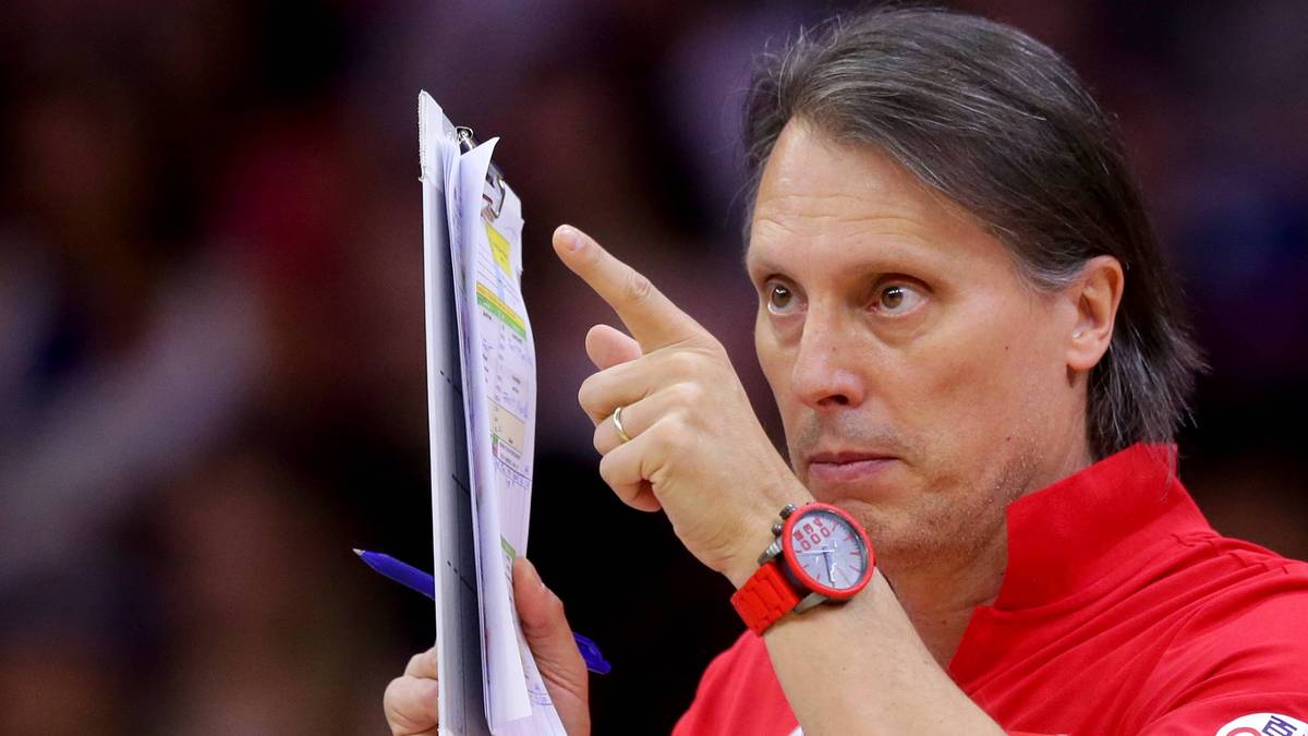 Mężczyzna w średnim wieku w czerwonej koszuli, wskazujący palcem na dokument z wykresami, z zegarkiem na nadgarstku.