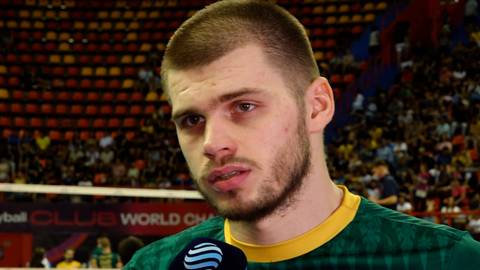 Portret mężczyzny, siatkarza Bartosza Kwoleka, na tle trybun hali sportowej.