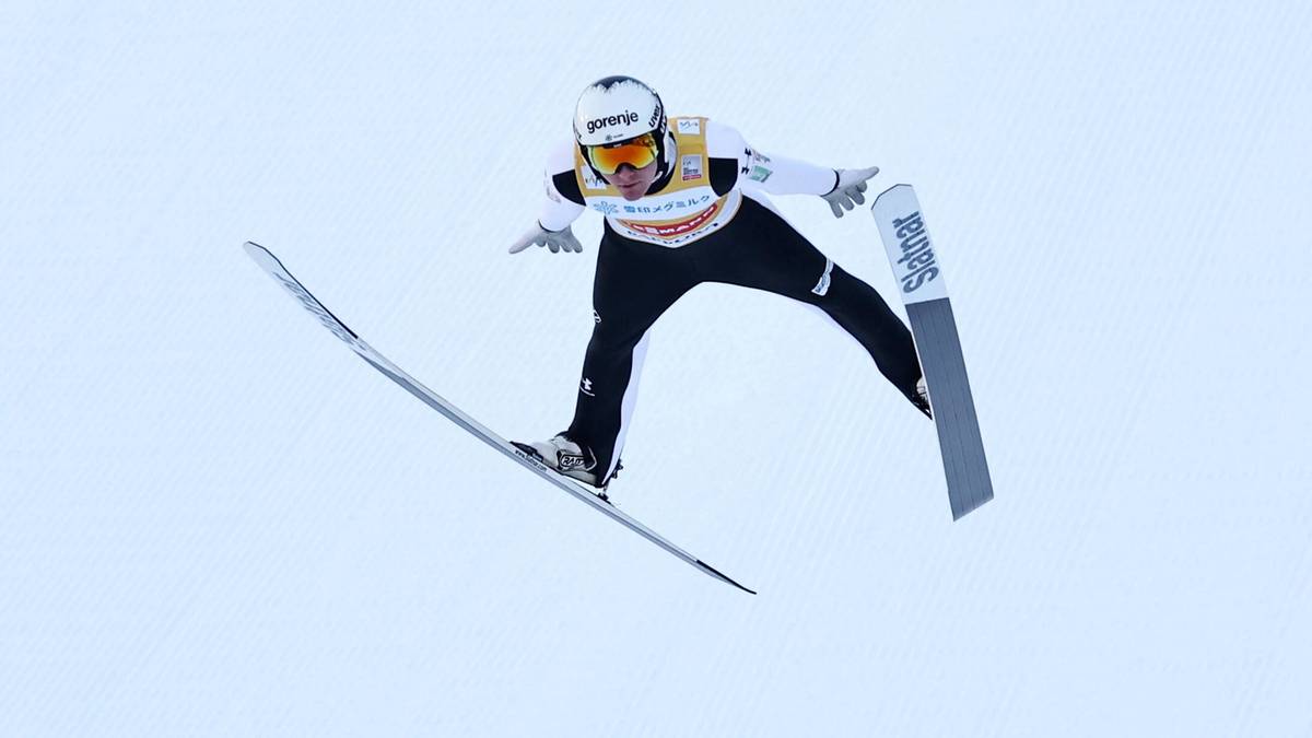 Skoczek narciarski w locie na tle jasnego, niebieskiego nieba.