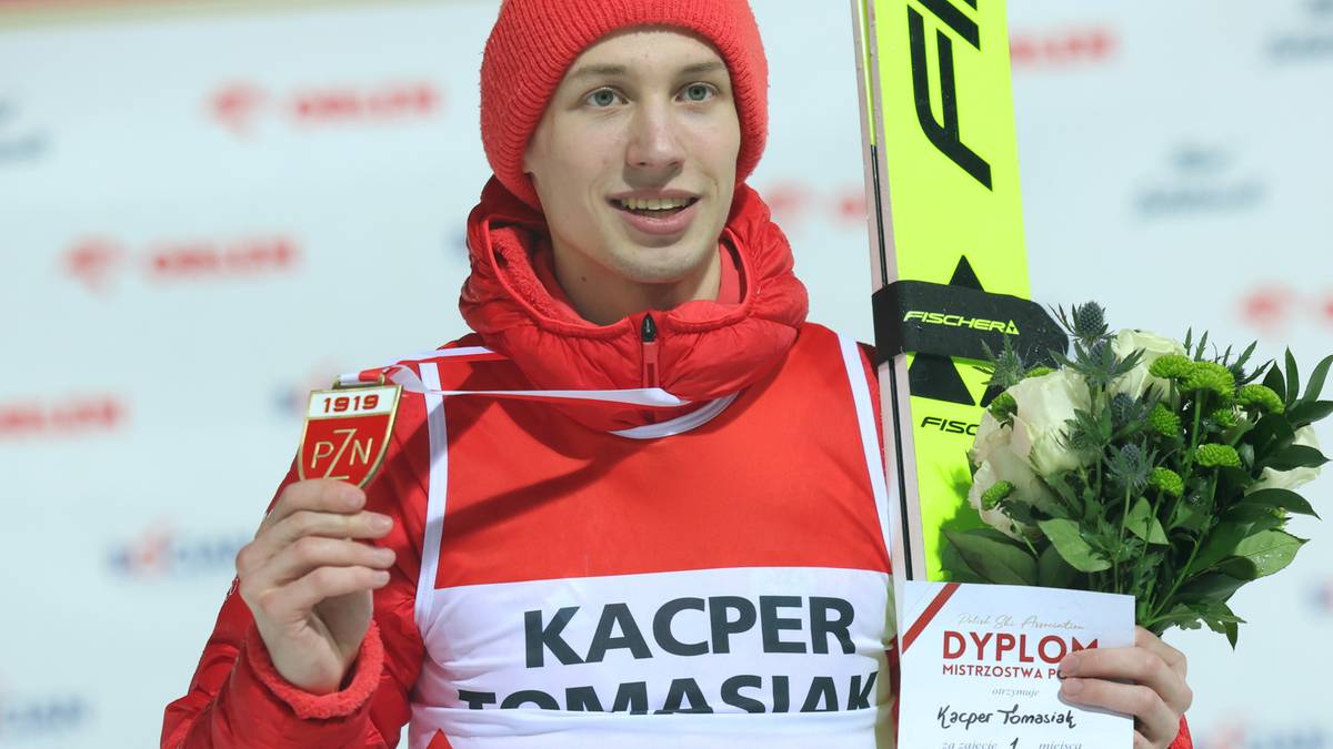 Skoczek narciarski Kacper Tomasiak w czerwonym stroju sportowym trzymający medal i dyplom.
