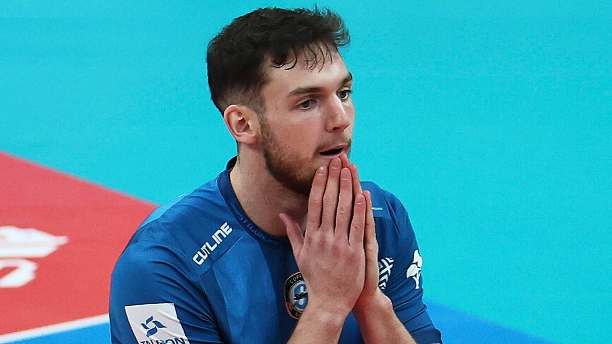 Dwóch siatkarzy w niebieskich strojach na boisku siatkarskim, jeden z dłońmi złożonymi przed twarzą.