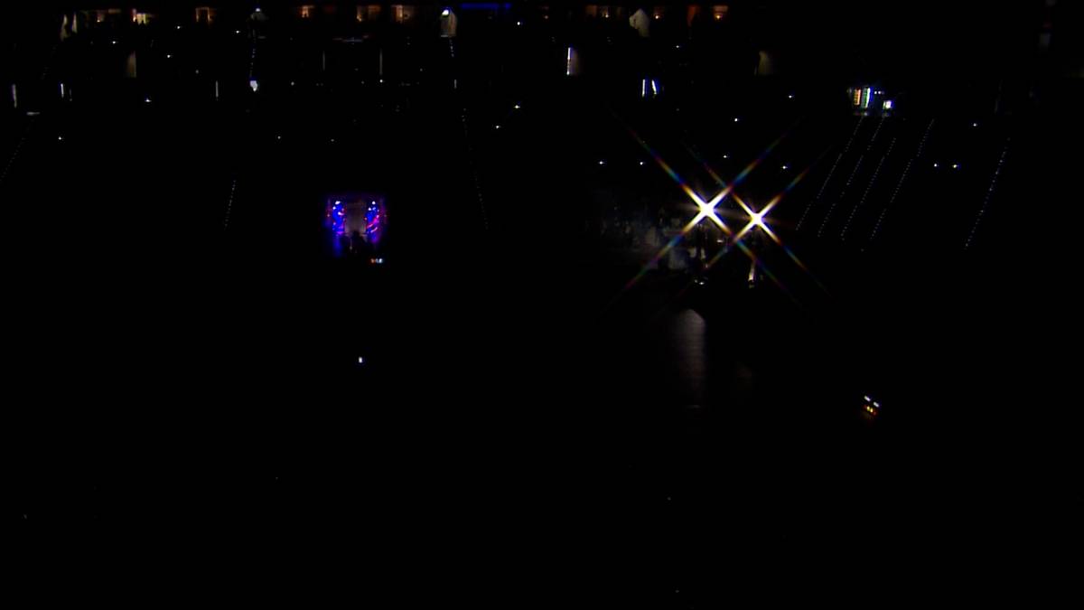 Ciemna hala sportowa z widocznymi światłami na trybunach i parkiecie, sugerująca przerwę w meczu siatkówki z powodu awarii oświetlenia.