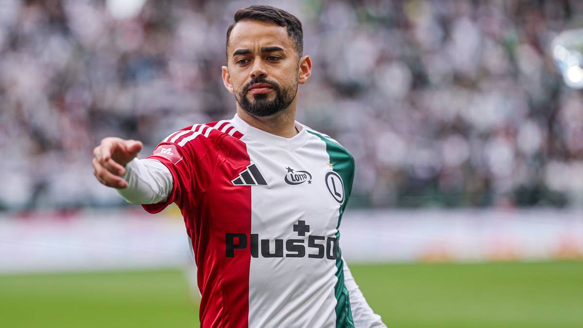 Piłkarz w czerwono-biało-zielonym stroju wskazuje palcem.