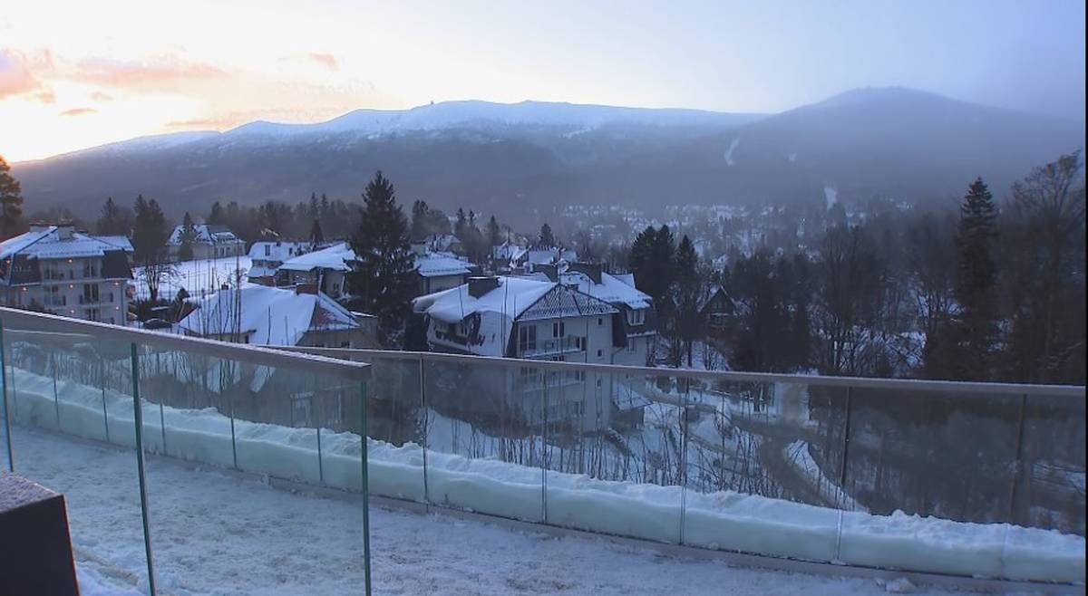 Krajobraz zimowy z ośnieżonymi domami i górami w tle.