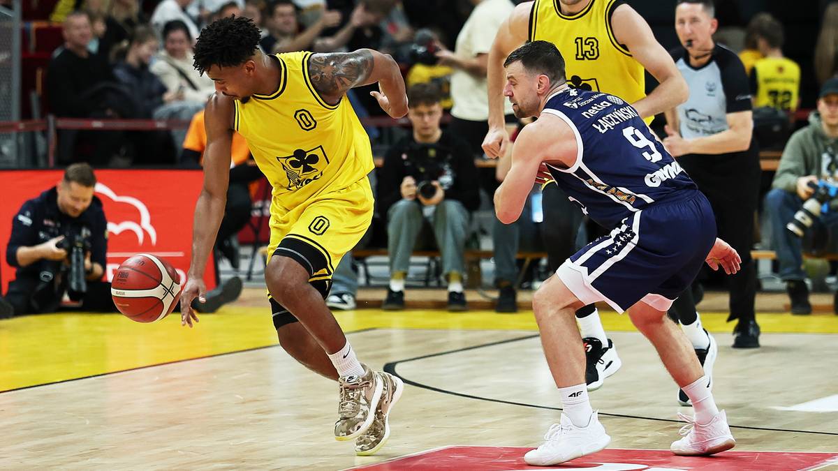 Koszykarz w żółtej koszulce z piłką przy nodze, broniony przez zawodnika w granatowej koszulce