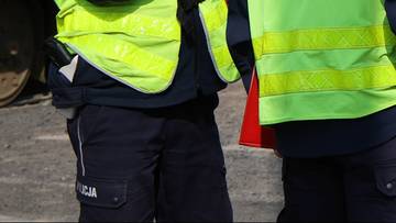 Dwóch mężczyzn w kamizelkach odblaskowych, jeden w czapce policyjnej, stoi obok żółtego tramwaju.