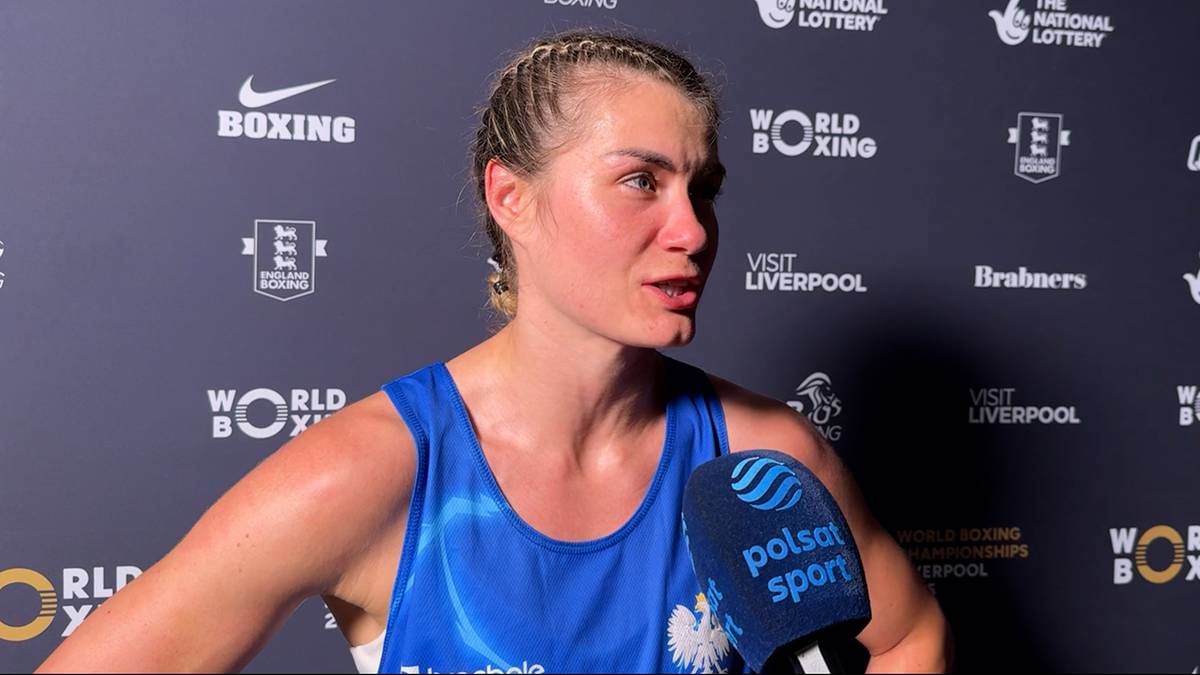 Portret bokserki z zaplecionymi włosami, z widoczną zmartwioną lub smutną miną, w niebieskim stroju sportowym, na tle ścianki z logotypami sponsorów.