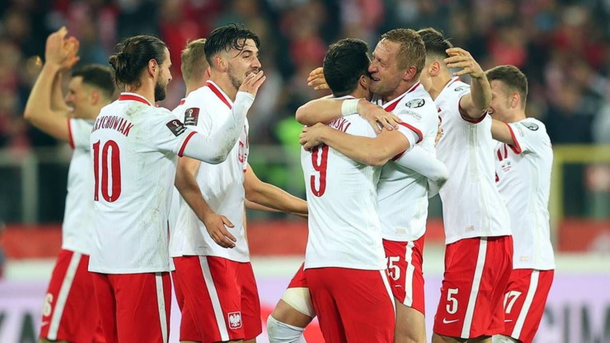 Piłkarze reprezentacji Polski w białych strojach, z czerwonymi elementami, celebrują zdobycie bramki, obejmując się nawzajem.