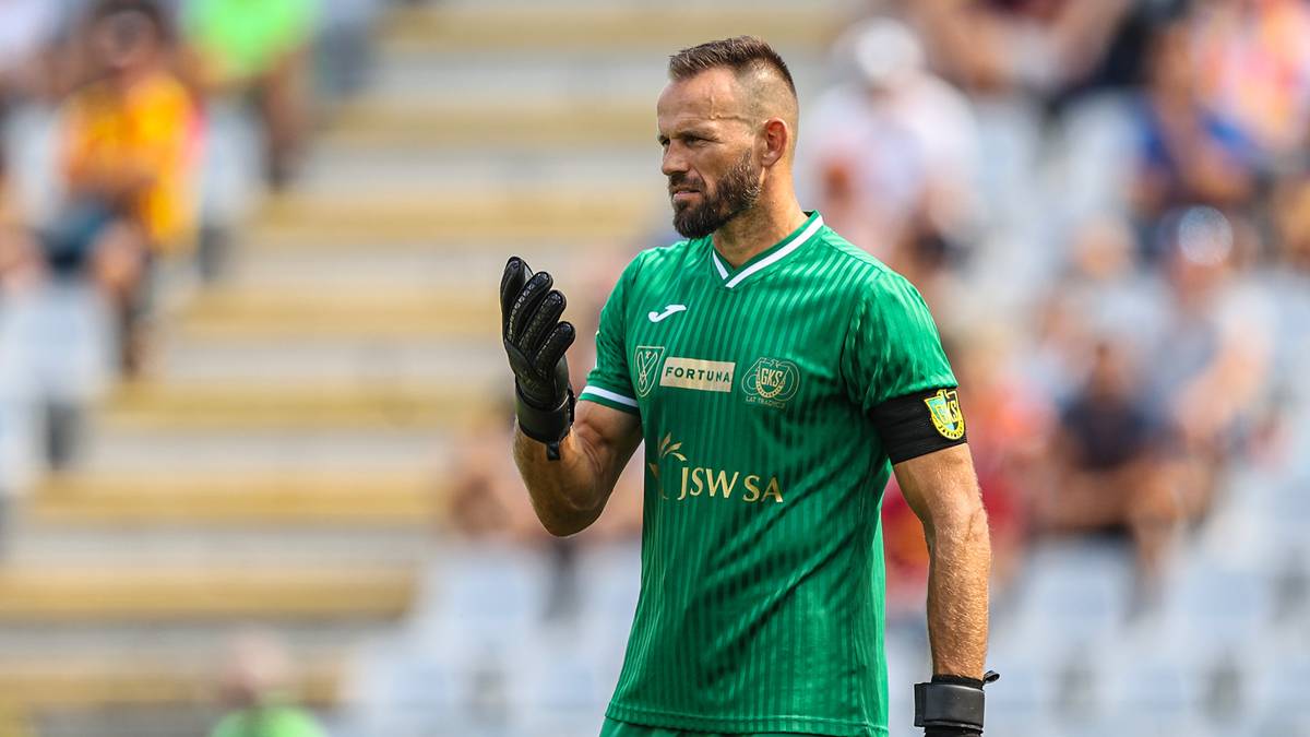 Piłkarz w zielonej koszulce bramkarskiej z rękawicami na rękach.