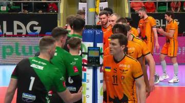 Siatkarze dw&oacute;ch drużyn zebrani wok&oacute;ł słupka siatki, część ubrana w zielono-czarne stroje, część w pomarańczowe.