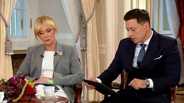 Kobieta w szarej marynarce i mężczyzna w garniturze siedzący w studiu telewizyjnym podczas rozmowy.