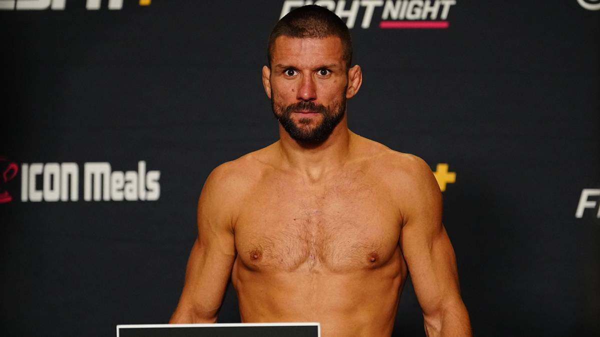 Mężczyzna o kr&oacute;tkich włosach i zaroście, o umięśnionej budowie ciała, stoi na tle czarnej ściany z logo "ICON Meals" i "FIGHT NIGHT".