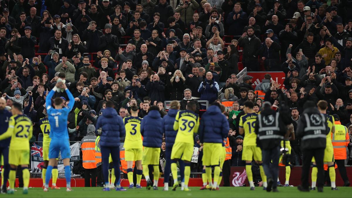 Tłum kibic&oacute;w na stadionie piłkarskim, niekt&oacute;rzy na murawie w strojach sportowych, inni na trybunach.