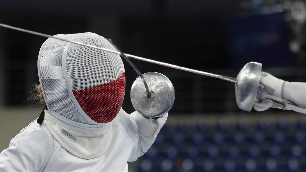 Szermierz w masce ochronnej z czerwoną siatką na twarzy celuje sztyletem do przeciwnika.