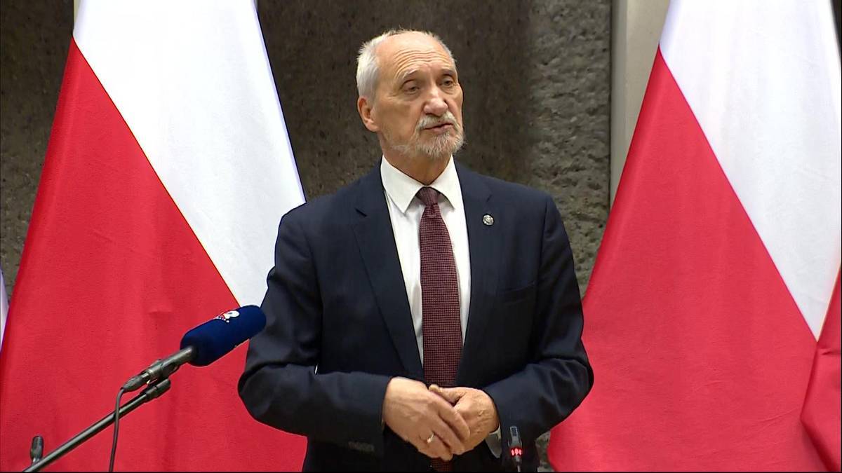 Antoni Macierewicz przemawia przed polskimi flagami.
