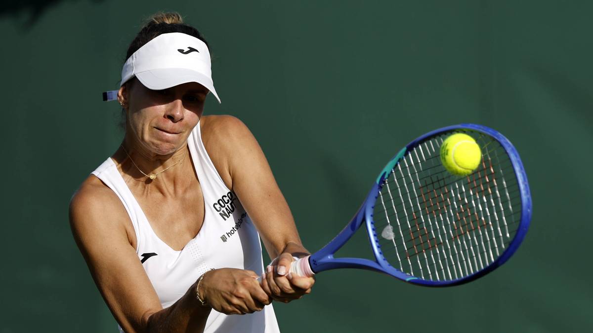 Tenisistka Magda Linette w białej koszulce i czapce z daszkiem odbija piłkę rakietą.