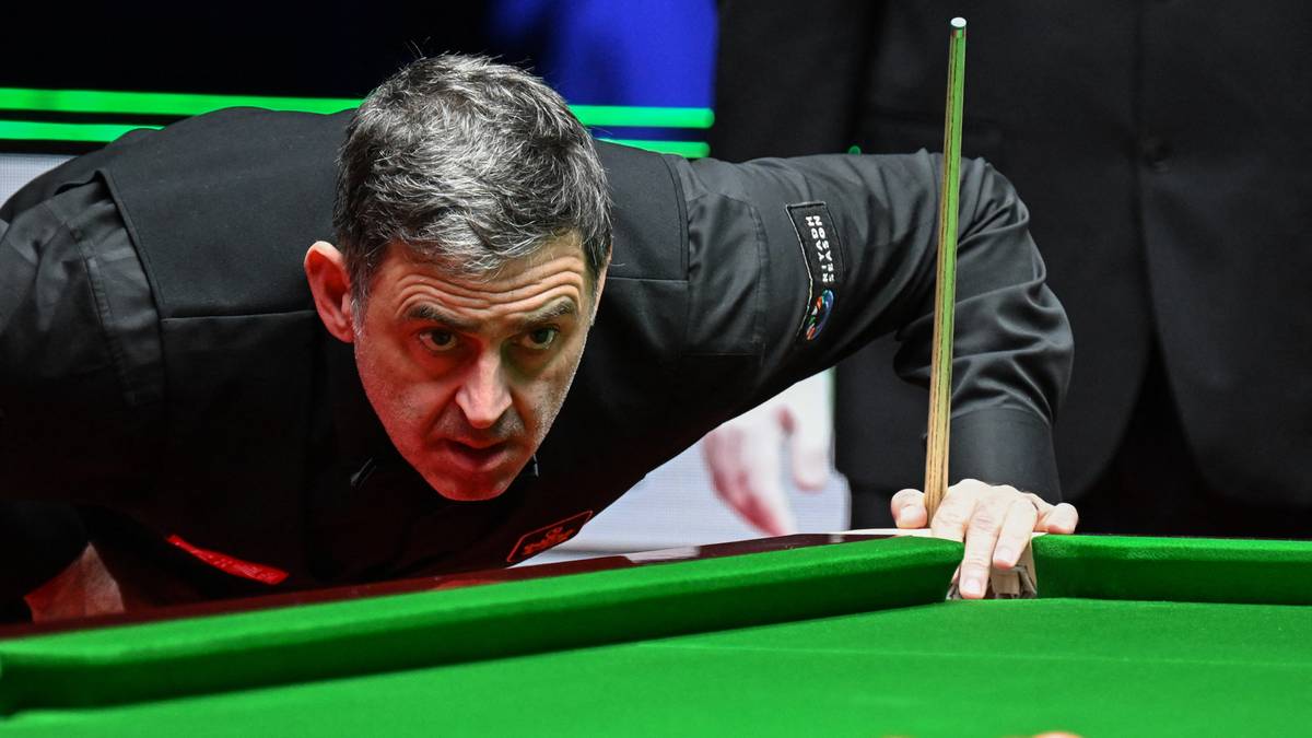 Snookerzysta Ronnie O'Sullivan pochylony nad zielonym stołem, celujący kijem w snookerowe bile.