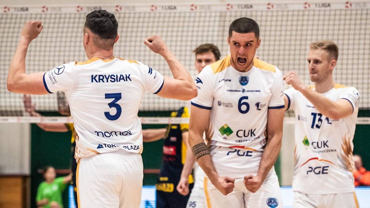 Siatkarze w białych strojach świętują zdobyty punkt, z uniesionymi rękami.