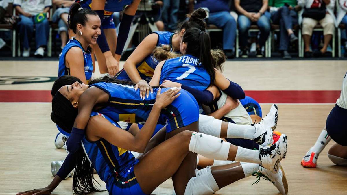 Grupa zawodniczek siatkówki w niebieskich strojach celebruje wygraną, tworząc emocjonalną "piramidę" radości na boisku.