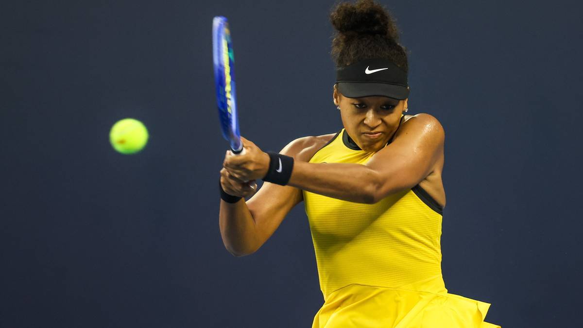 Naomi Osaka w ż&oacute;łtej sukience tenisowej wykonuje uderzenie forhendowe podczas meczu, z piłką w locie.