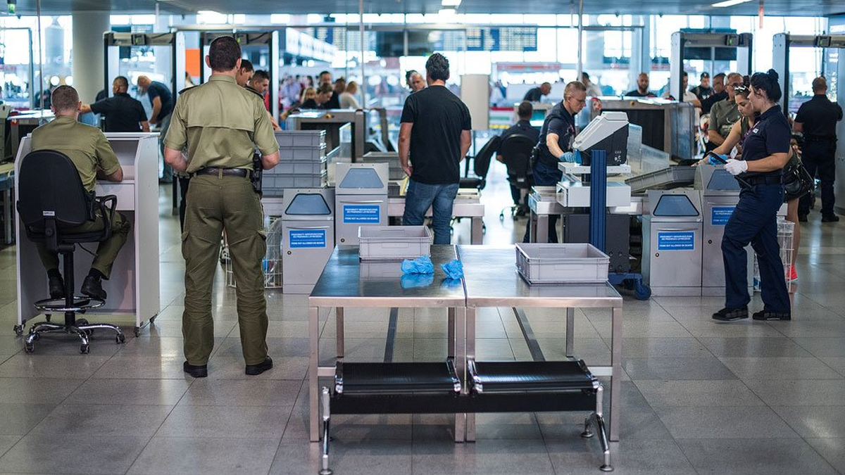 Kontrola bezpieczeństwa na lotnisku z celnikami i podr&oacute;żnymi przechodzącymi przez bramki.
