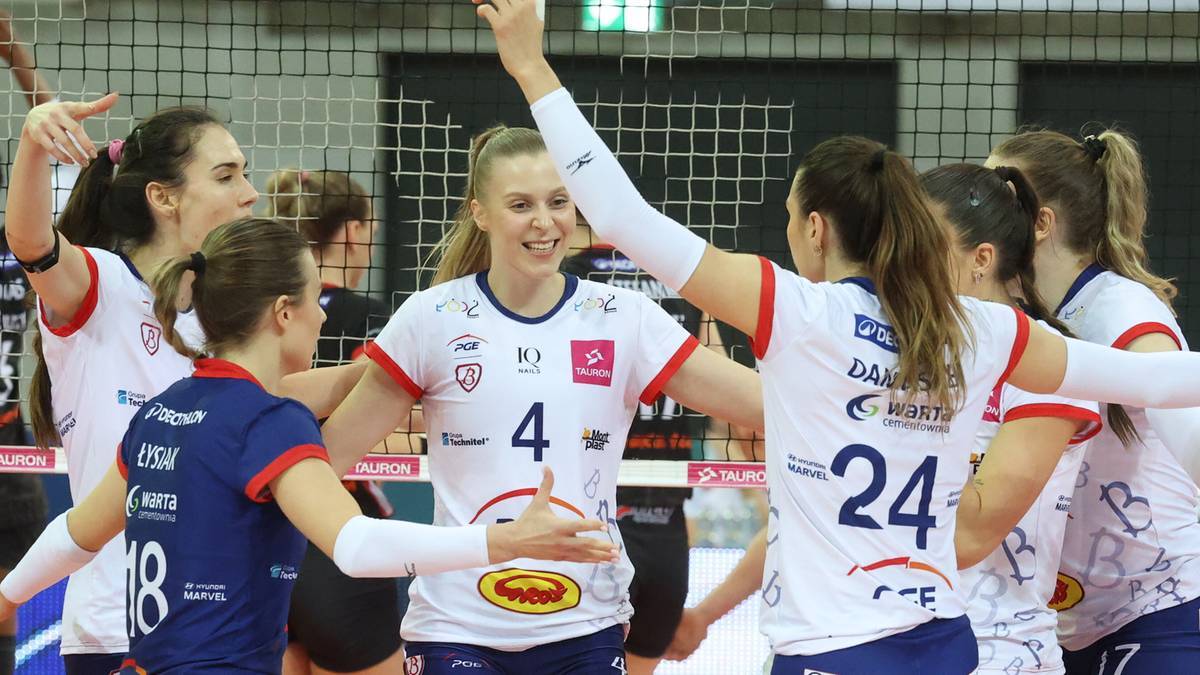 Grupa siatkarek w białych strojach świętuje zdobyty punkt, jedna z nich podnosi ręce do g&oacute;ry, inne się śmieją i przytulają.