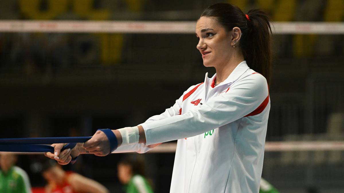 Kobieta w białej bluzie sportowej z czerwonymi pasami ćwiczy z taśmą oporową.