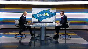 Dw&oacute;ch mężczyzn siedzi przy stole w studiu telewizyjnym przed ekranem z logo programu.