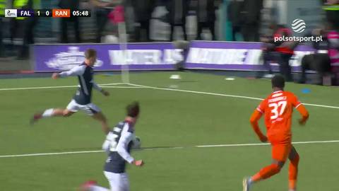 Trzech zawodnik&oacute;w na boisku piłkarskim podczas meczu. Dw&oacute;ch w białych i granatowych strojach, jeden w pomarańczowym.