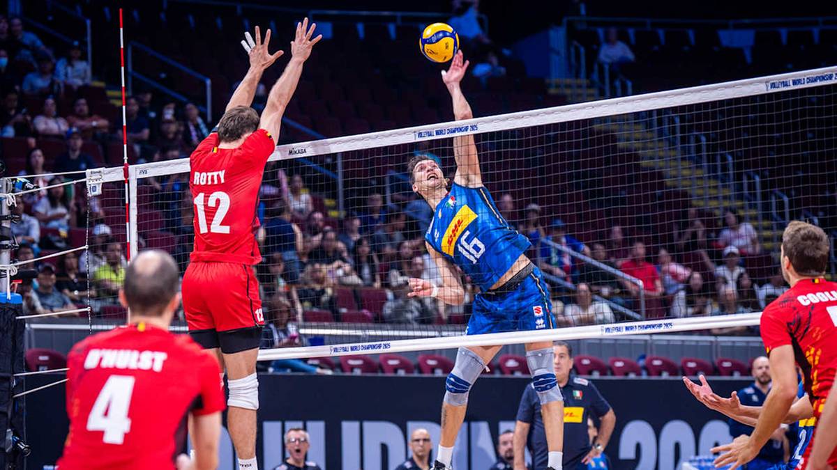 Siatkarz w niebieskim stroju wyskakuje do zagrania piłki nad siatką, drugi siatkarz w czerwonym stroju próbuje go zablokować.