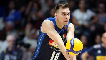 Siatkarz w niebieskiej koszulce z numerem 16 i niebieskimi spodenkami wykonuje odbicie piłki w meczu siatk&oacute;wki.