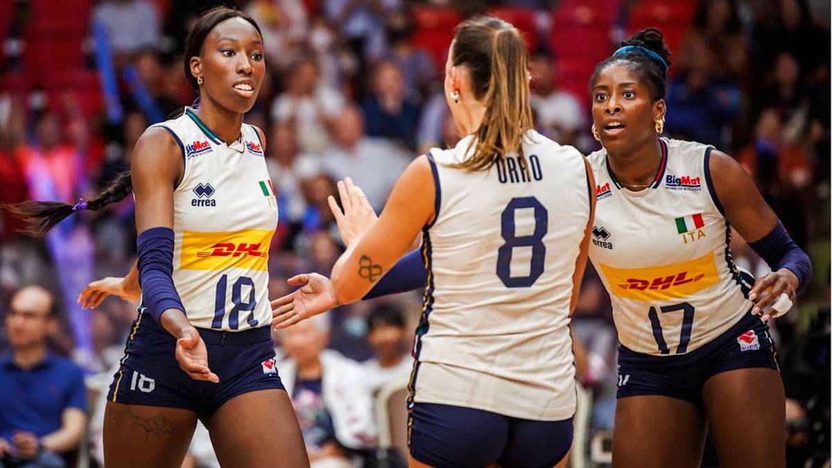 Trzy siatkarki w białych koszulkach i granatowych spodenkach podczas meczu siatkówki.