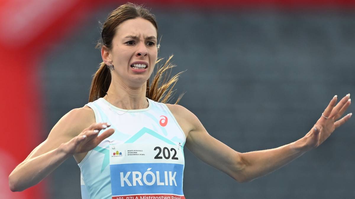 Lekkoatletka w białej koszulce z numerem 202 i napisem "KR&Oacute;LIK" na piersi podczas biegu, z wykrzywioną z b&oacute;lu twarzą i uniesionymi rękami.