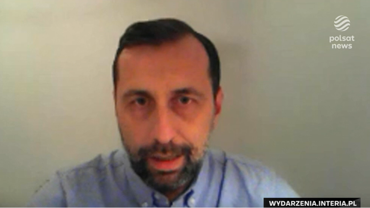 Mężczyzna w niebieskiej koszuli z kr&oacute;tkim zarostem patrzy w kamerę.