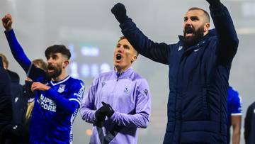 Trzech piłkarzy w piłkarskich strojach świętuje z podniesionymi rękami.