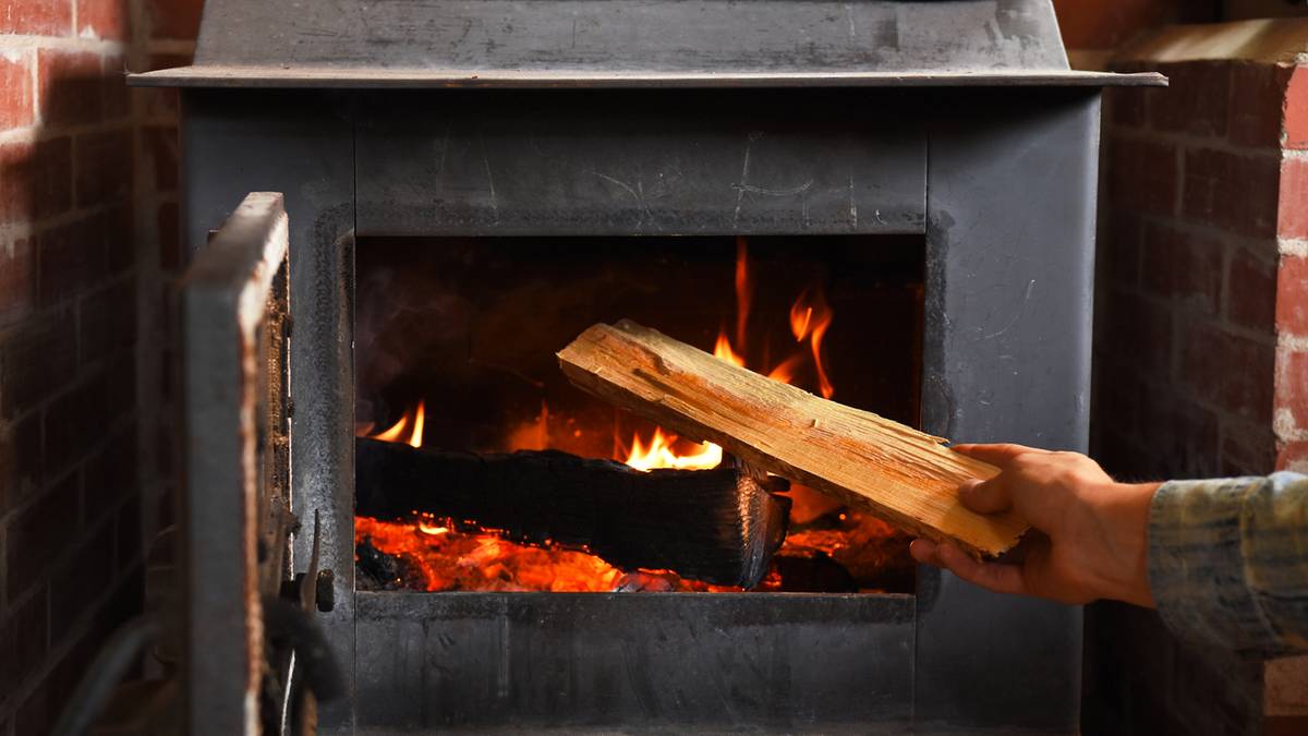 Dłoń wkłada drewno do płonącego kominka.