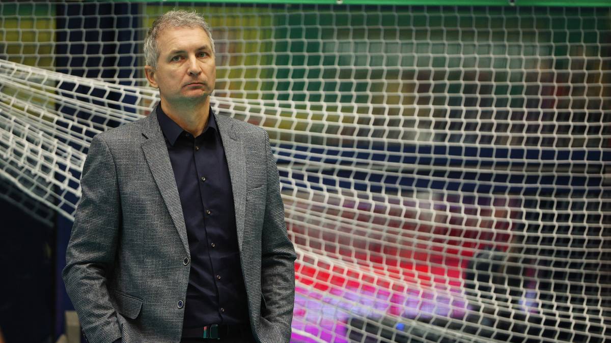Trener siatk&oacute;wki Andrzej Kowal stoi na tle siatki, patrząc w bok.