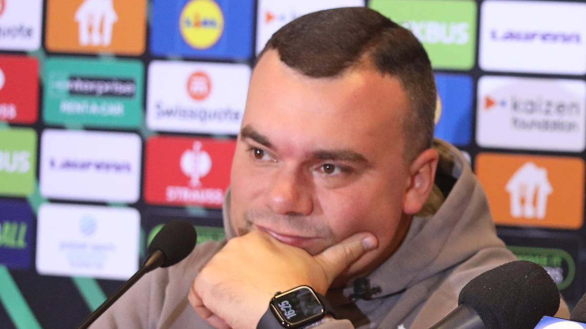 Dwóch mężczyzn siedzi przy stole podczas konferencji prasowej z mikrofonami i butelkami wody.