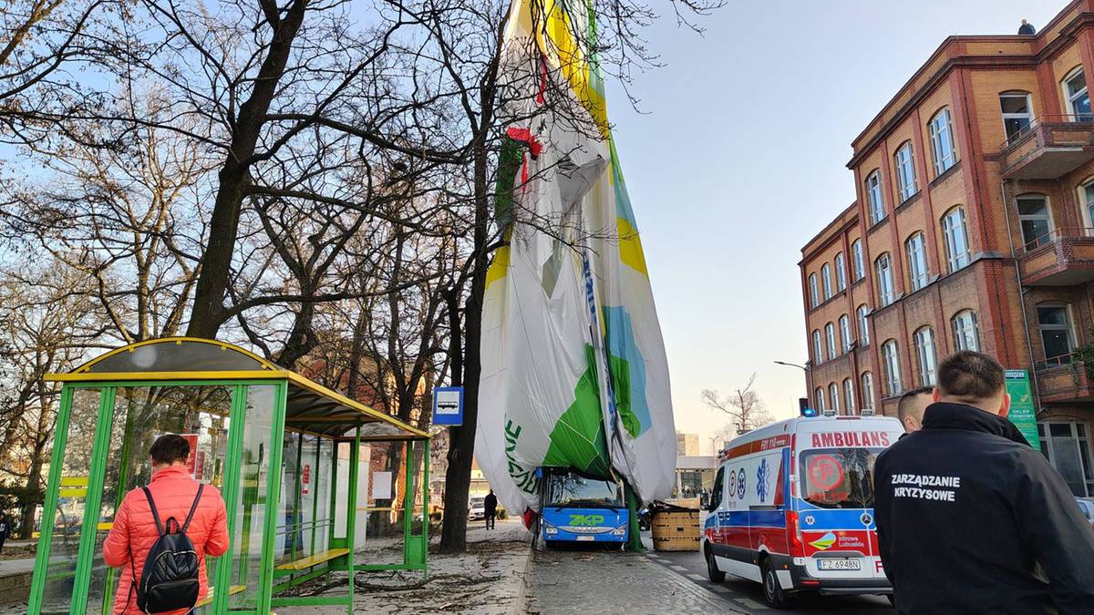 Rozbity balon z koszem, widoczny fragment budynku, karetka pogotowia i inne pojazdy ratunkowe.