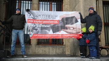 Transparent z napisem "TA 'STREFA' nie czyści powietrza, tylko portfele!" trzymany przez dwie osoby dorosłe z dziećmi.