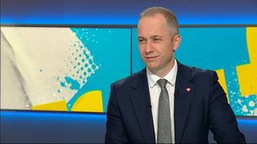 Polityk w garniturze i krawacie, patrzący w bok, na tle ekranu z kolorowymi abstrakcyjnymi wzorami.