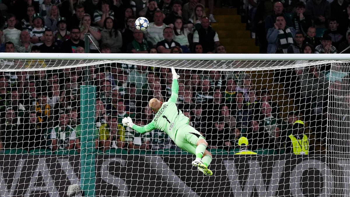 Bramkarz w zielonym stroju wykonuje efektowny rzut w kierunku piłki nad bramką podczas meczu.