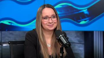 Kobieta w okularach siedzi przed mikrofonem, uśmiecha się.