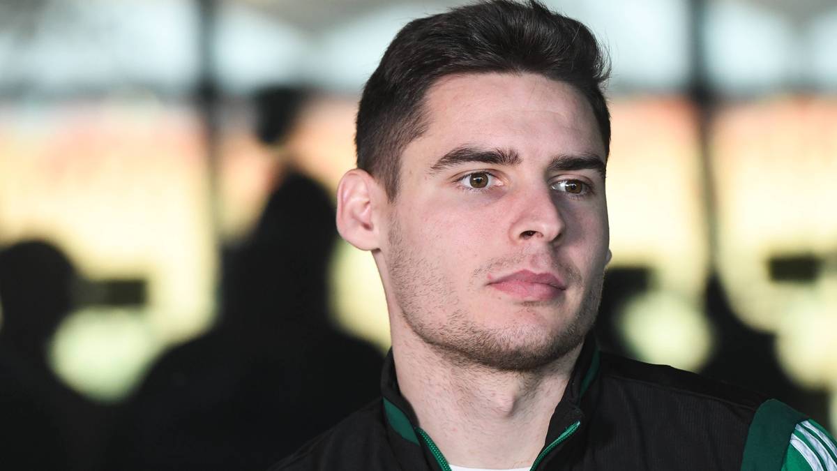 Portret młodego mężczyzny, zwięzłe włosy, lekki zarost, patrzący w bok. Nosi ciemną kurtkę z zielonymi wstawkami.