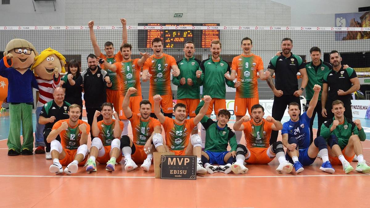 Drużyna siatkarzy w strojach pomarańczowo-zielonych pozuje do zdjęcia, z zawodnikiem trzymającym tabliczkę MVP.