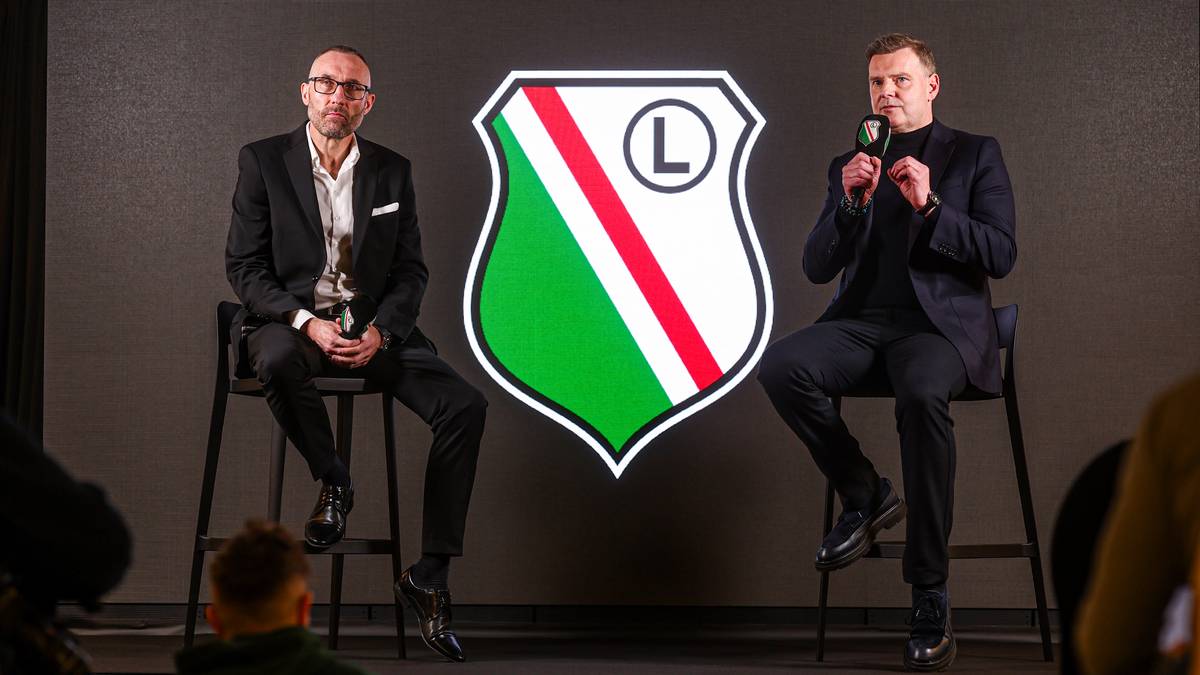 Dw&oacute;ch mężczyzn siedzi na krzesłach przed logo Legii Warszawa podczas konferencji prasowej.