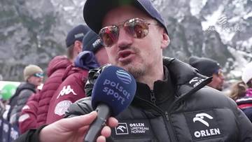 Adam Małysz, ubrany w czapkę z daszkiem i okulary przeciwsłoneczne, m&oacute;wi do mikrofonu Polsat Sport. W tle widoczni są inni ludzie oraz g&oacute;ry.