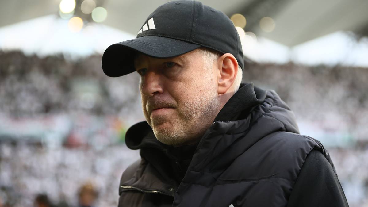 Trener piłkarski w czapce z daszkiem i czarnym ubraniu, patrzący w bok.